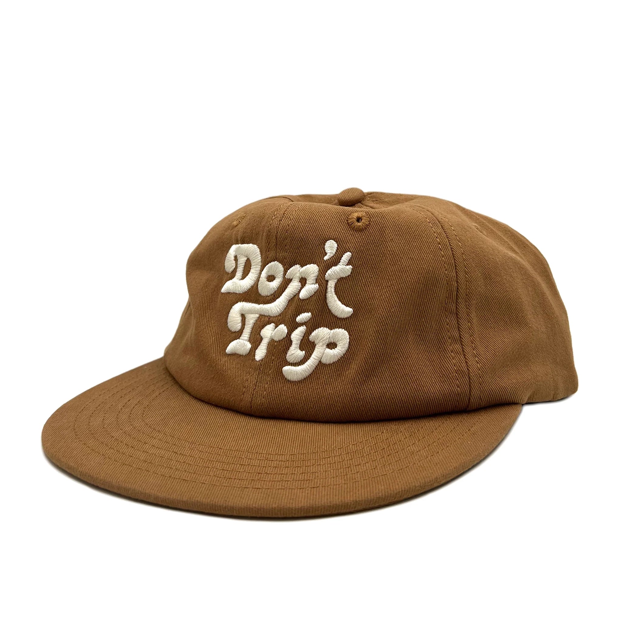 On a white background is a brown unstructured 6 panel baseball hat with white embroidery that reads, &quot;Don&#39;t Trip&quot;.