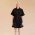 On a tan background is a model wearing a black zip up dress with short sleeves and a collar. 