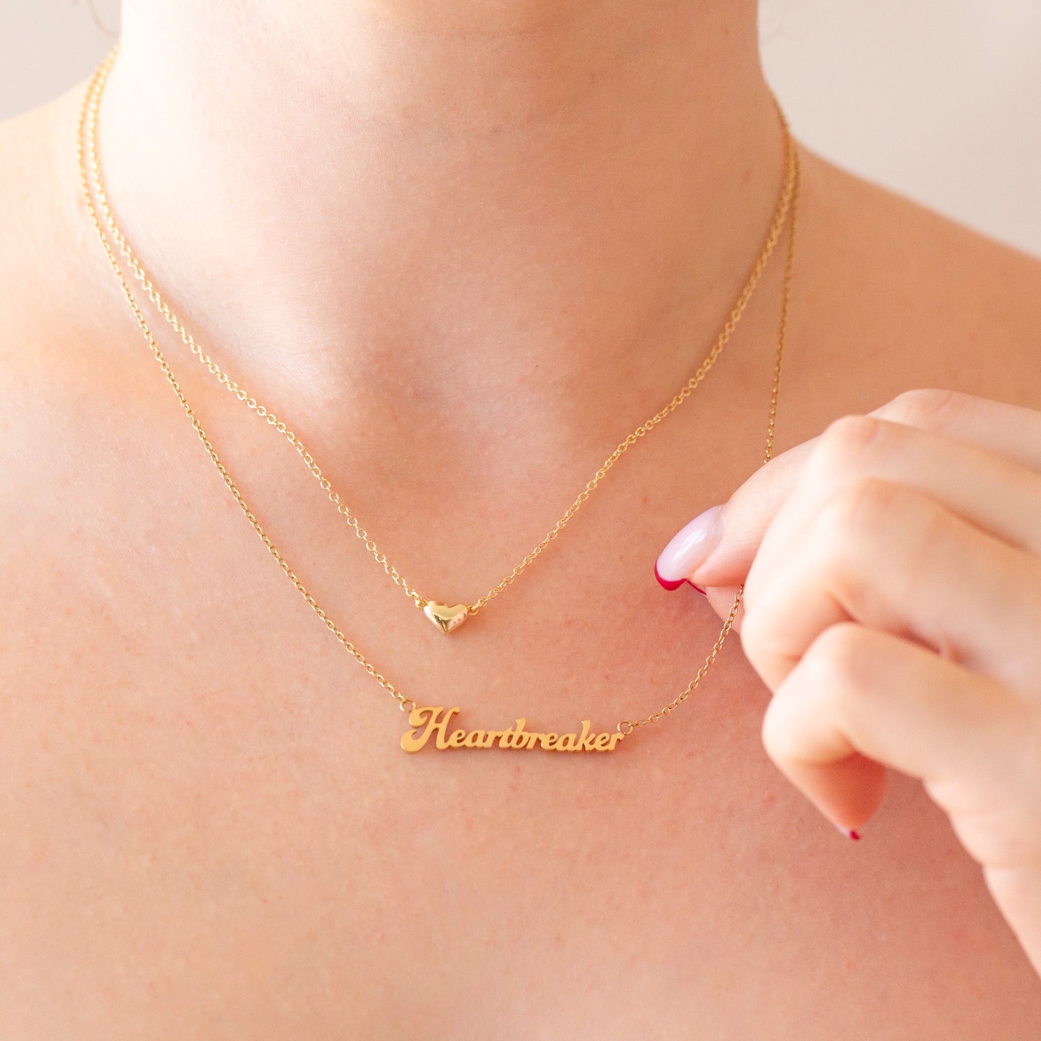 A gold name plate style necklace that reads, "Heartbreaker". 