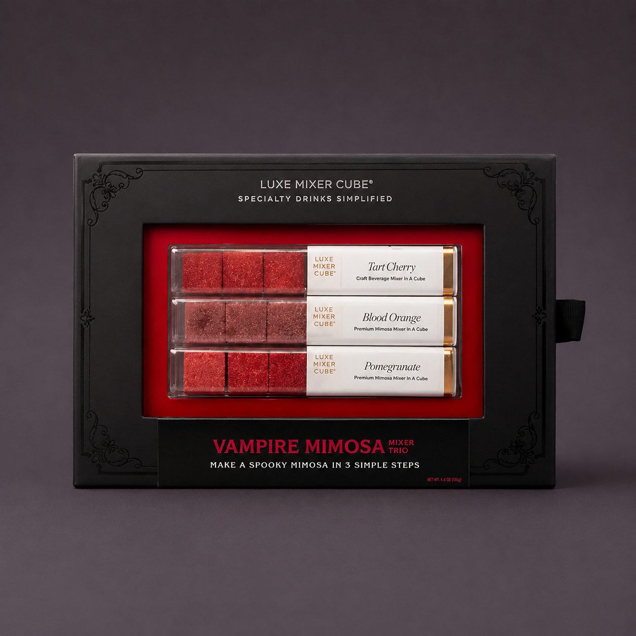 Luxe Mixer Cube Vampire Mimosa flavor kit in a black presentation box with a red interior window, showing three red drink cubes labeled Tart Cherry, Blood Orange, and Pomegranate on a dark gray background.