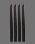 A set of four black taper candles with with dark pinkish purple wax that drips when the candles are lit. 