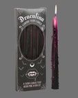 A set of four black taper candles with with dark pinkish purple wax that drips when the candles are lit. 