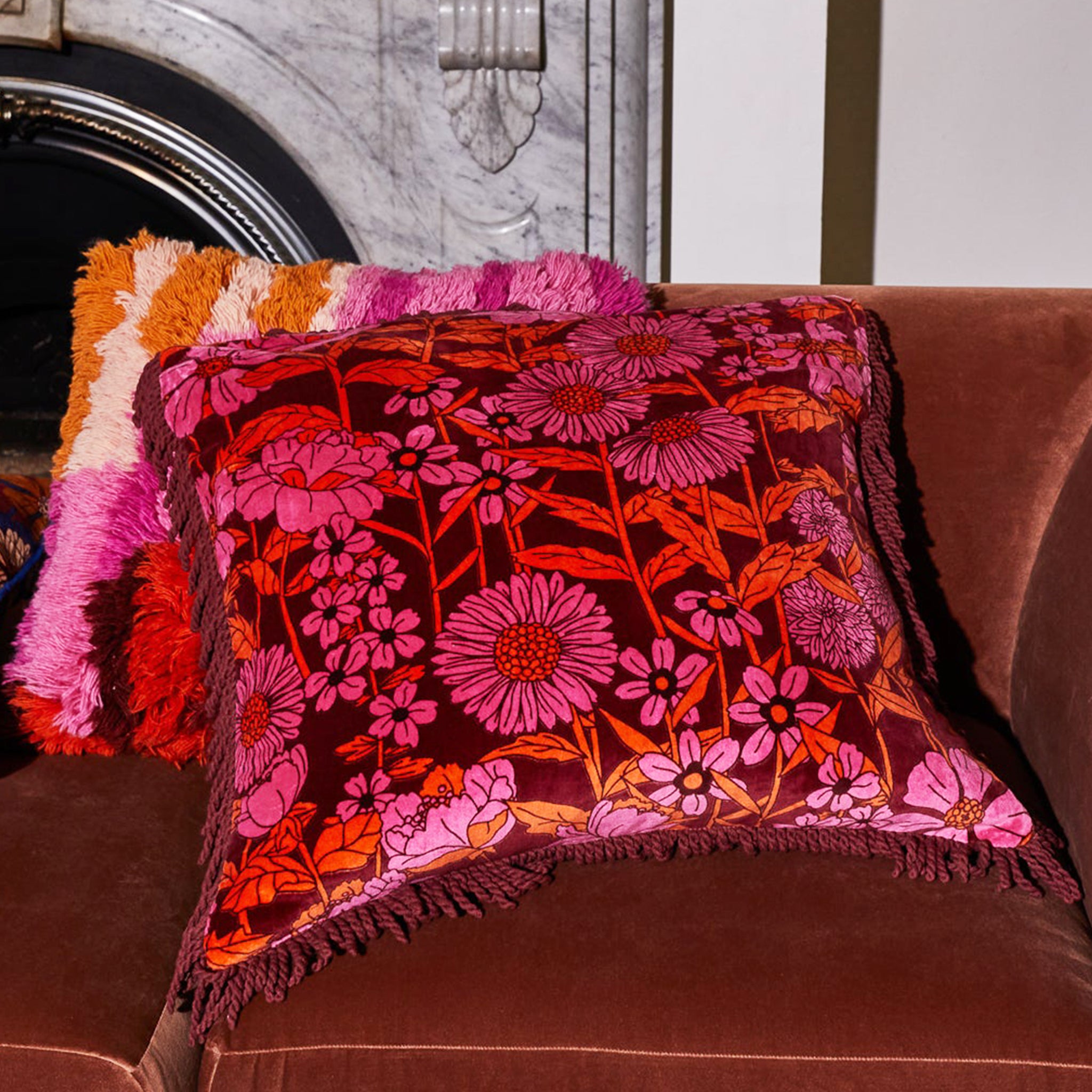 A pink and orange floral printed pillow with a fringe detail.