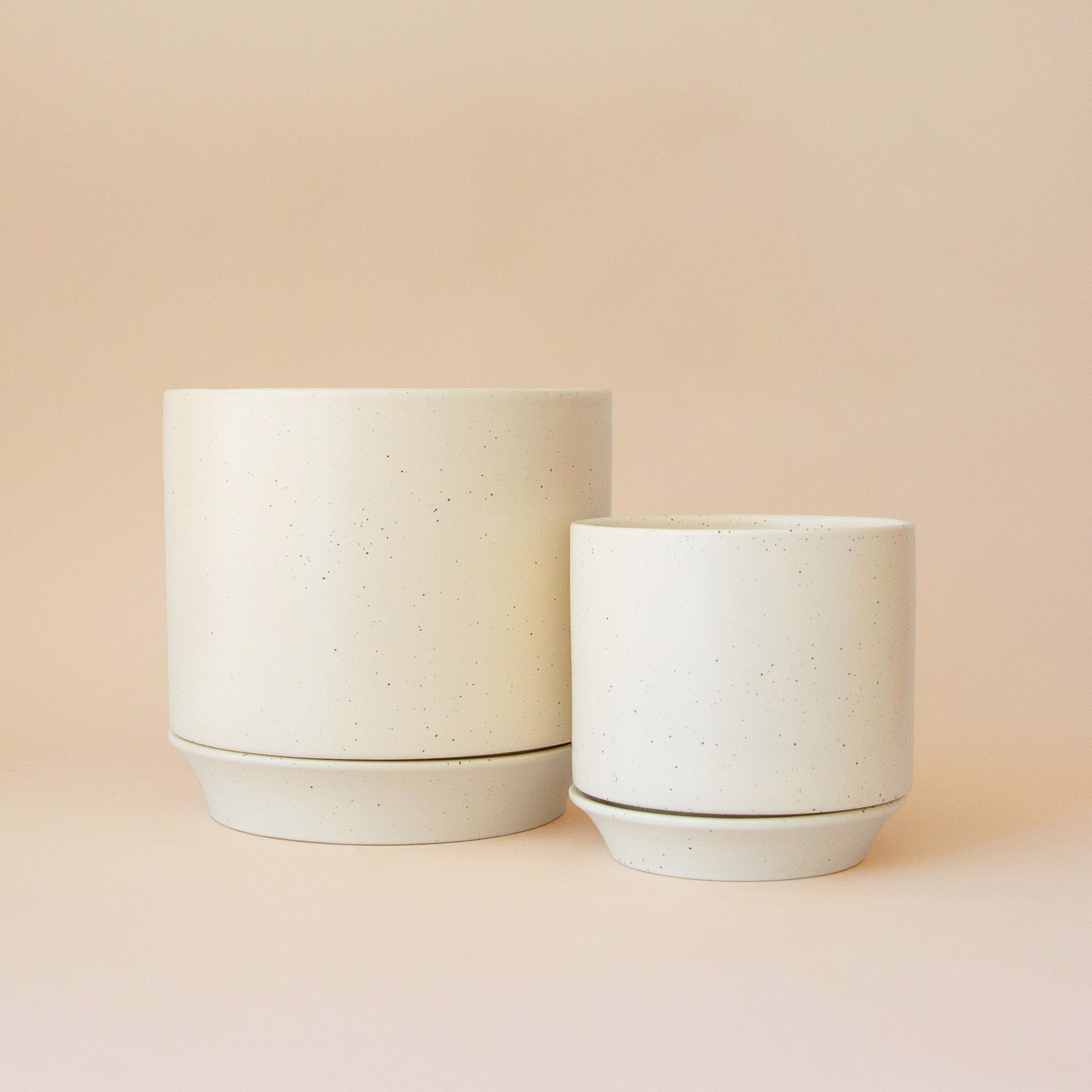 Two white pots with speckle detail on a peach background.