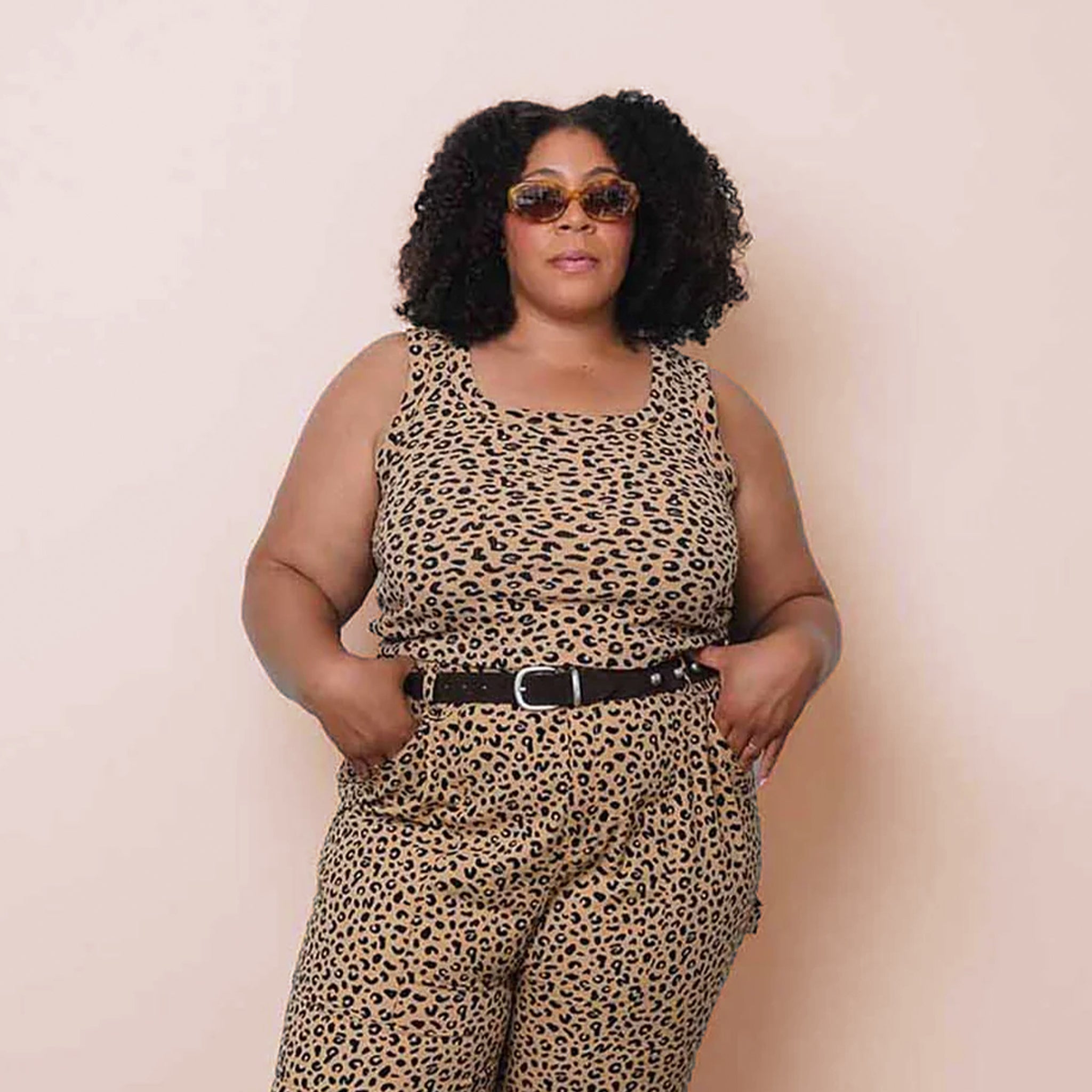 Woman wearing a leopard print tank top with a belt against a beige background
