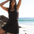 Girl wearing matching top and bottoms in black waffle fabric.  She stands in front of a beach with her arms up over her head.