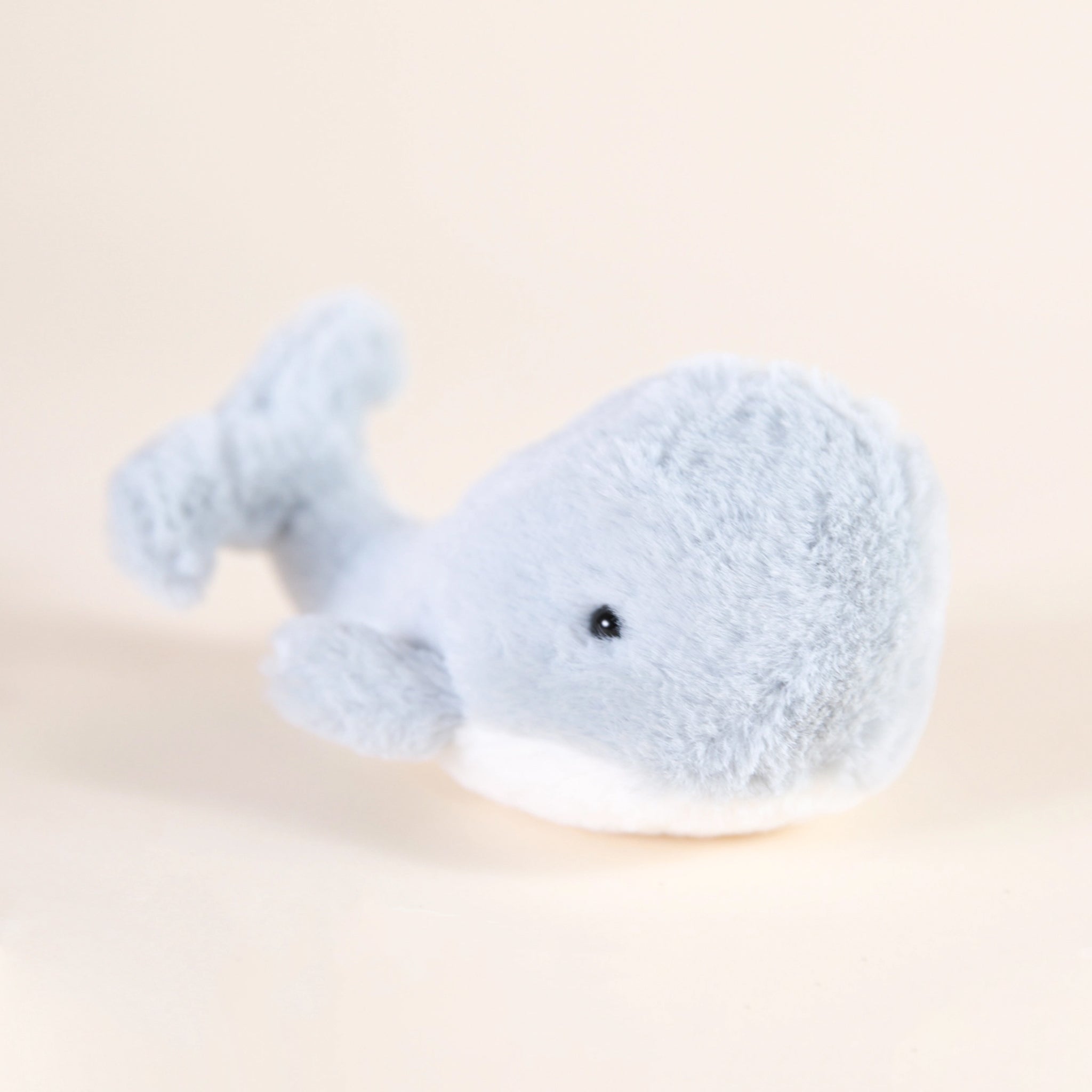A light blue/gray whale stuffed animal with a fuzzy texture and a split tail and black friendly beaded eyes.