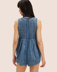 A model wearing a short denim romper with a v-neck and string tie in the center. 