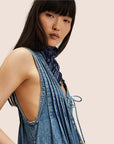 A model wearing a short denim romper with a v-neck and string tie in the center. 