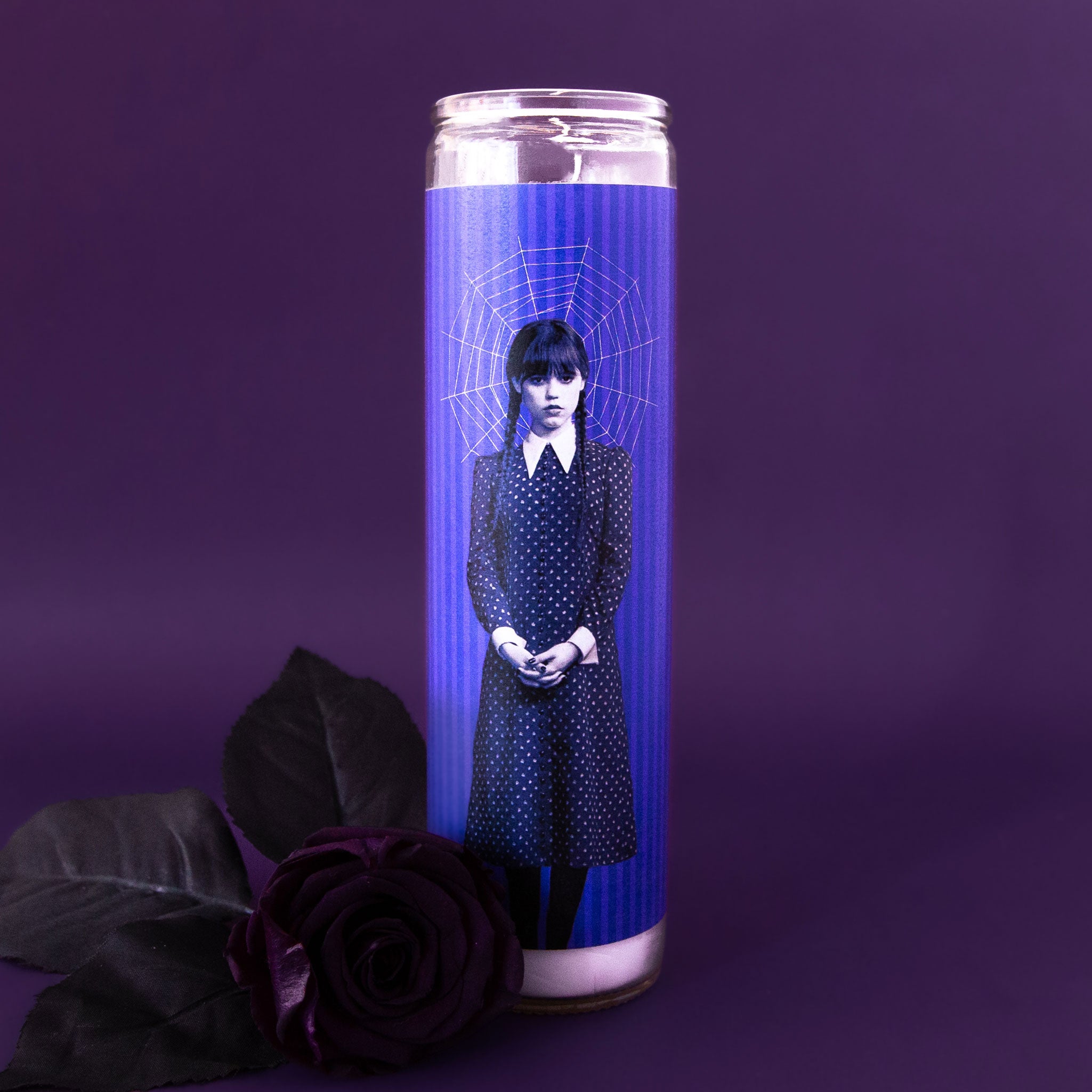 A prayer candle with a label that has a photo of Wednesday Adams. 