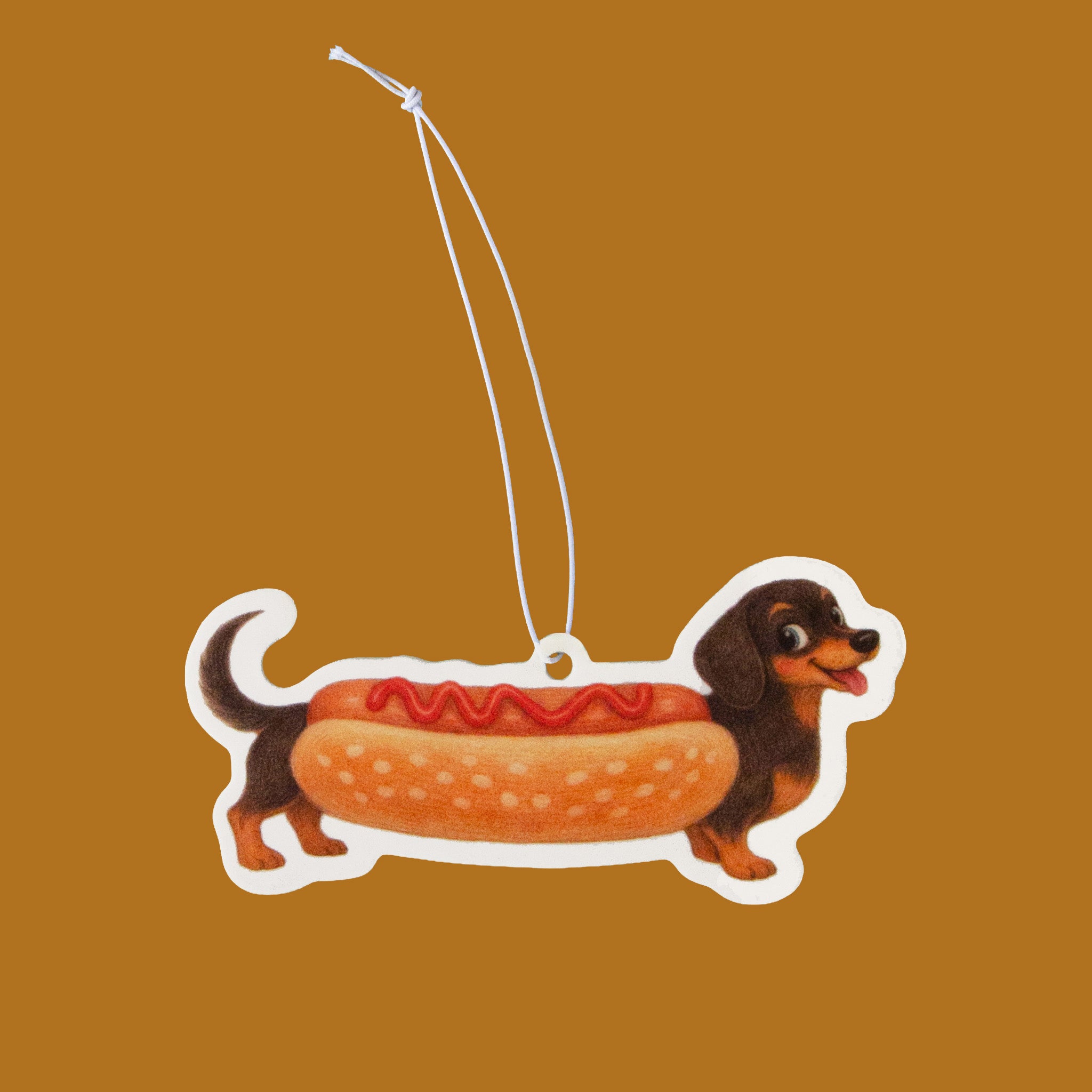 A packaged Halloween air freshener shaped like a dachshund dressed as a hot dog, shown in a clear plastic bag with an orange header card that reads 'Halloweenie Air Freshener.'.