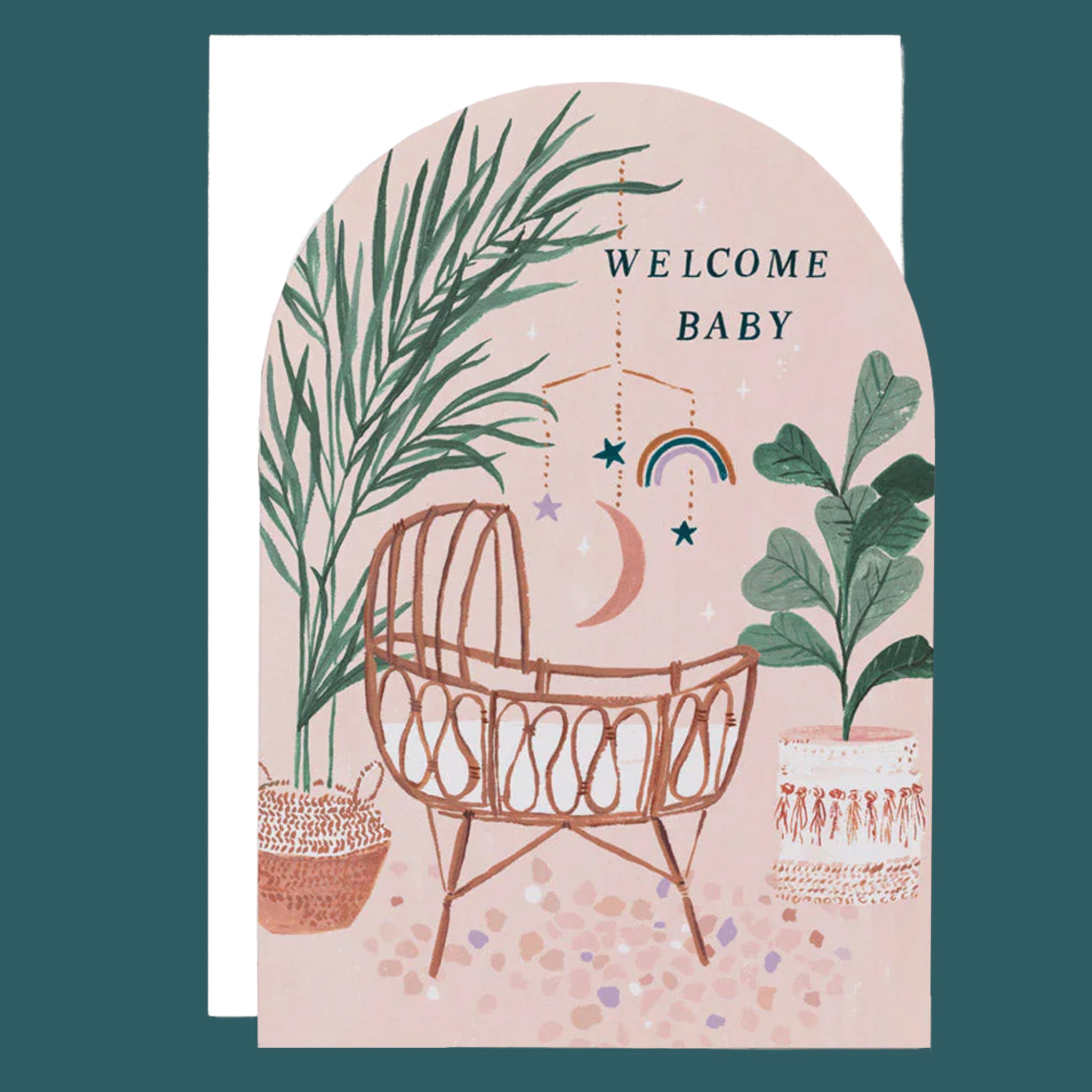 An arched greeting card with a sunset desert color pallet along with an illustration of a woven rattan baby&#39;s crib along with bohemian illustrations of lush natural foliage, bamboo, palm trees, and dried flowers and text at the top that reads, &quot;Welcome Baby&quot; in black letters.