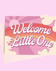 On a light purple background is a greeting card featuring a rainbow and sun graphic and white text in the center that reads, "Welcome Little One".