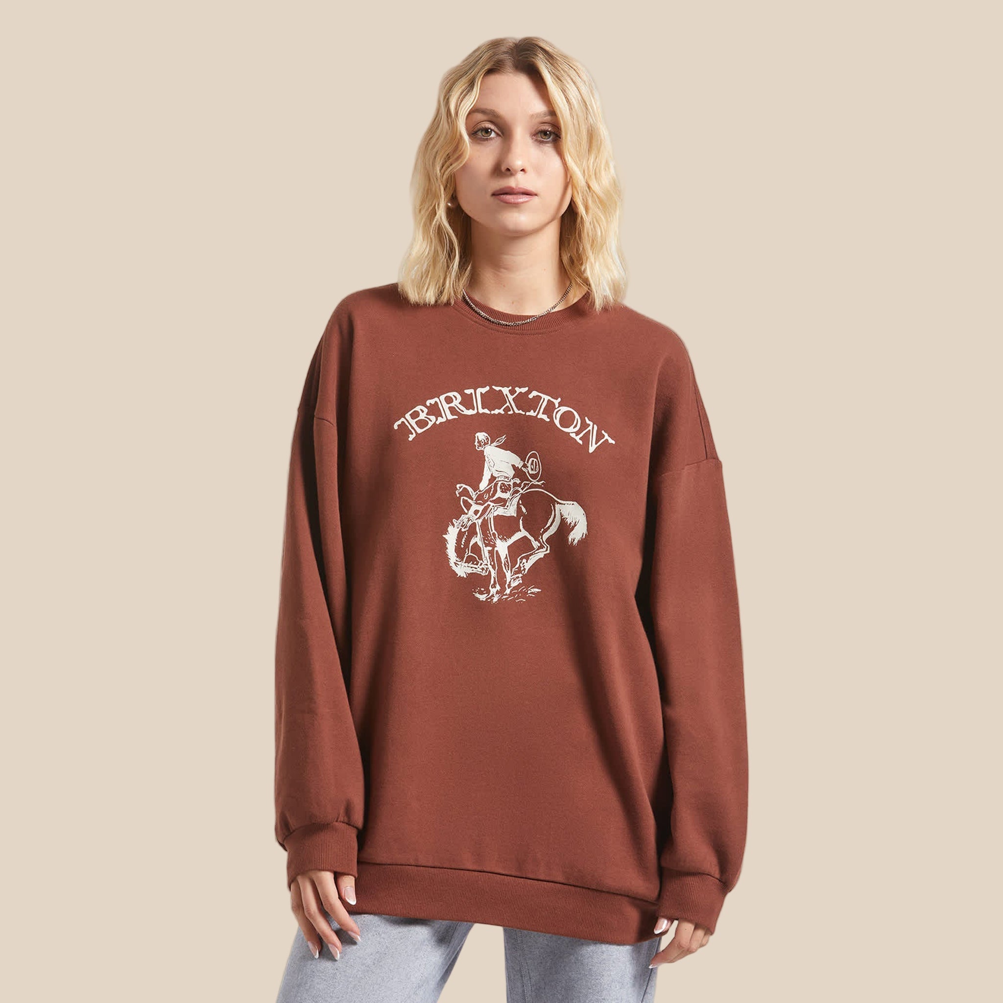 A rust colored crew neck sweatshirt with cream colored text that reads, "Brixton" with a graphic of a cowboy on a bucking horse. 