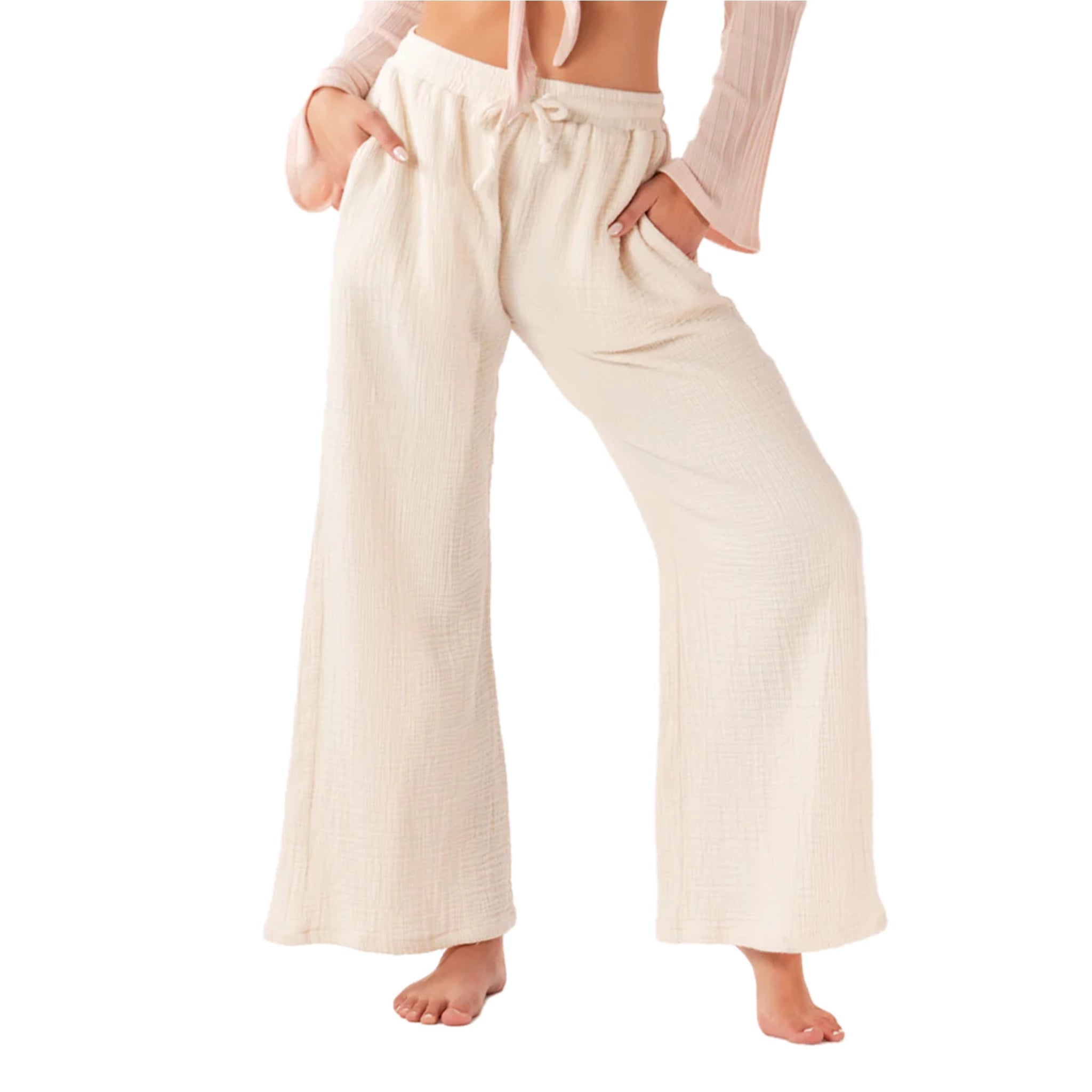 On a white background is a model wearing cream wide leg pants with a drawstring and pockets. 