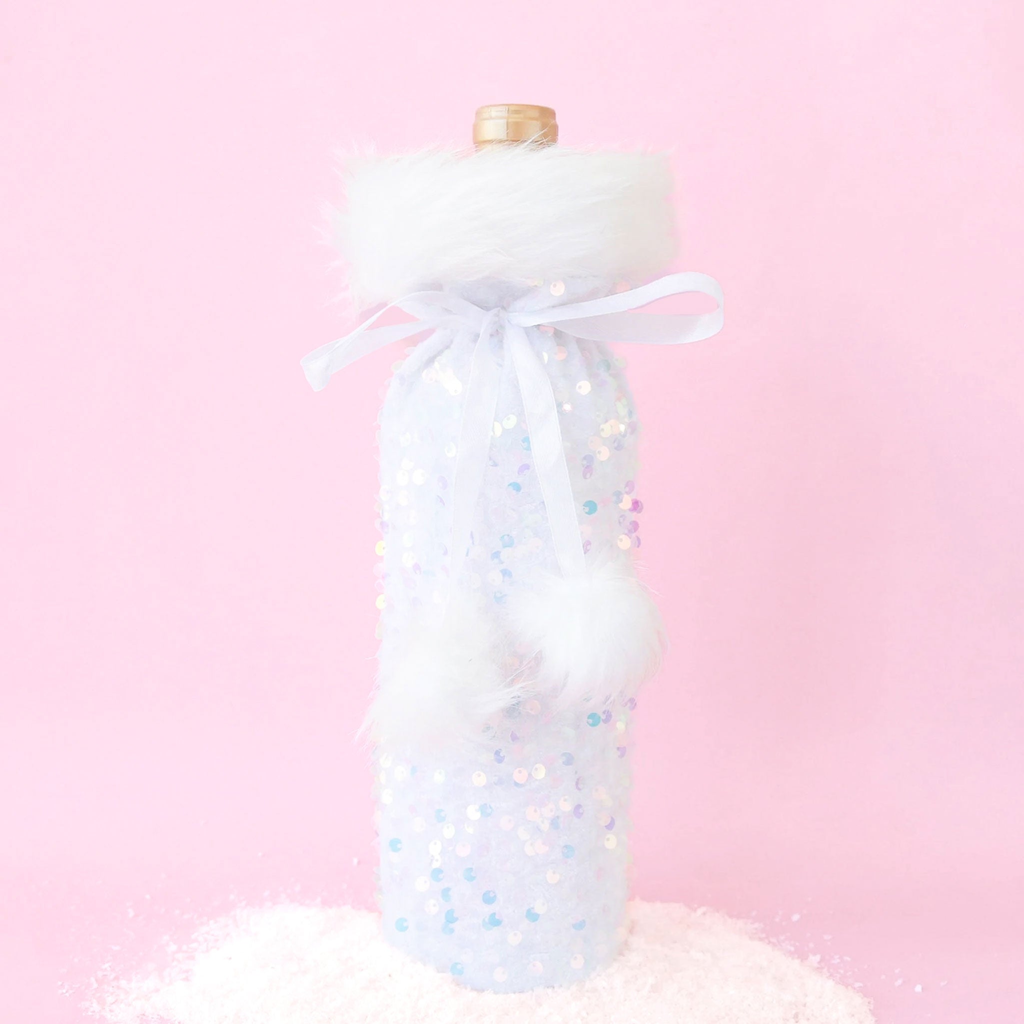 On a pink background is a iridescent and white wine bag with fluffy white faux fur lining the top and a pom pom bow to tie.  