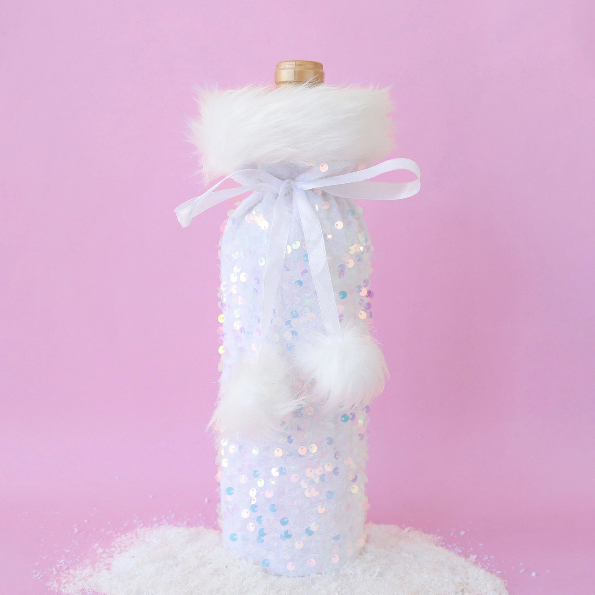 On a purple background is a iridescent and white wine bag with fluffy white faux fur lining the top and a pom pom bow to tie.