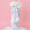 On a pink background is a silver sequin wine gift bag with white faux fur around the opening and a white pom pom bow around the top. 