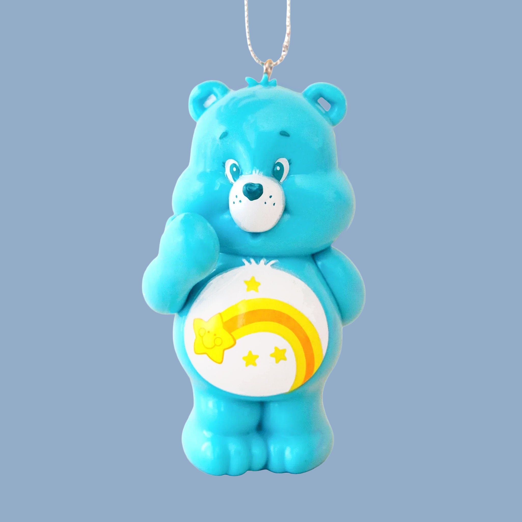 On a blue background is a blue care bear shaped glass ornament with a yellow shooting star on its stomach. 