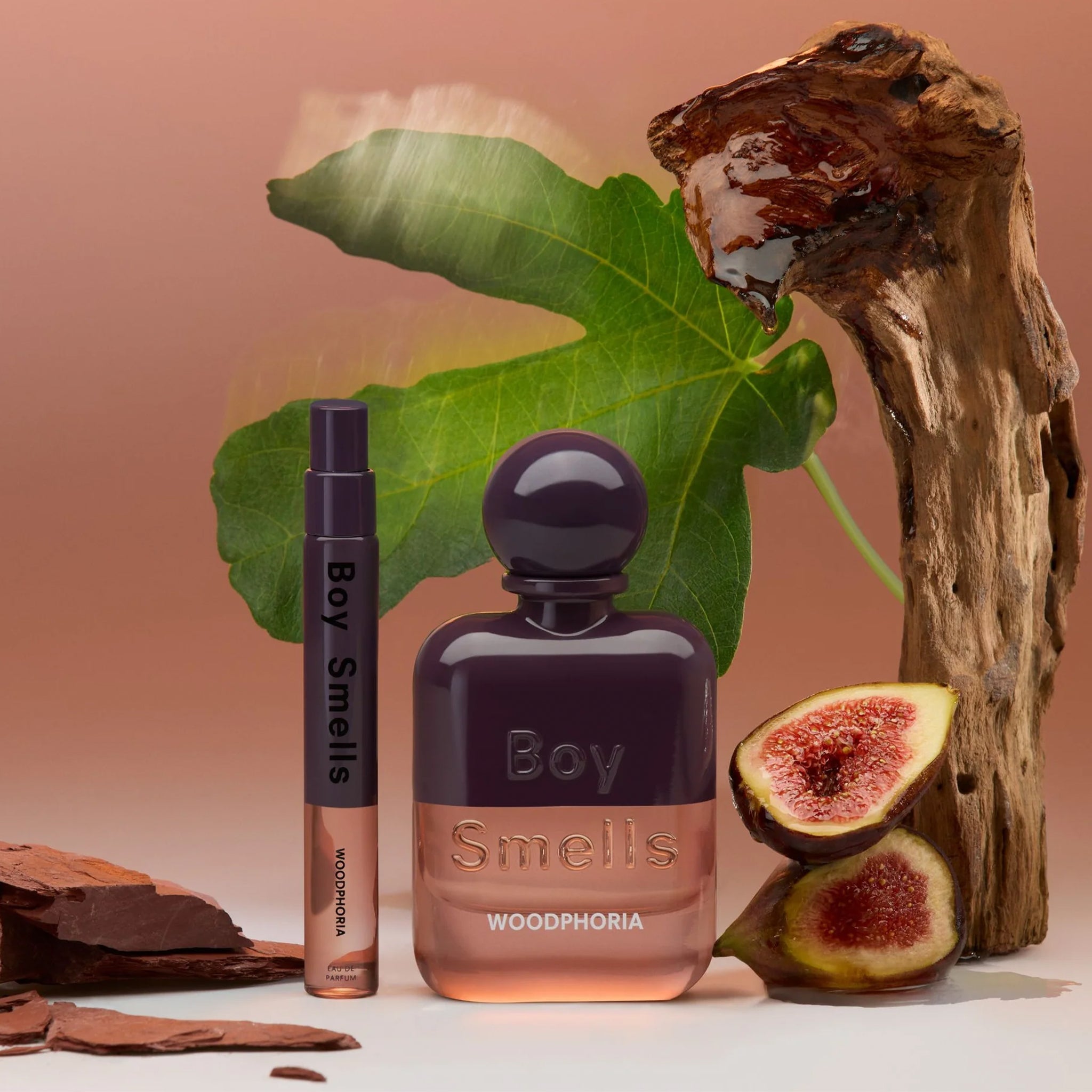 A perfume bottle that is purple and light pink and text that reads, "Boy Smells Woodphoria". 