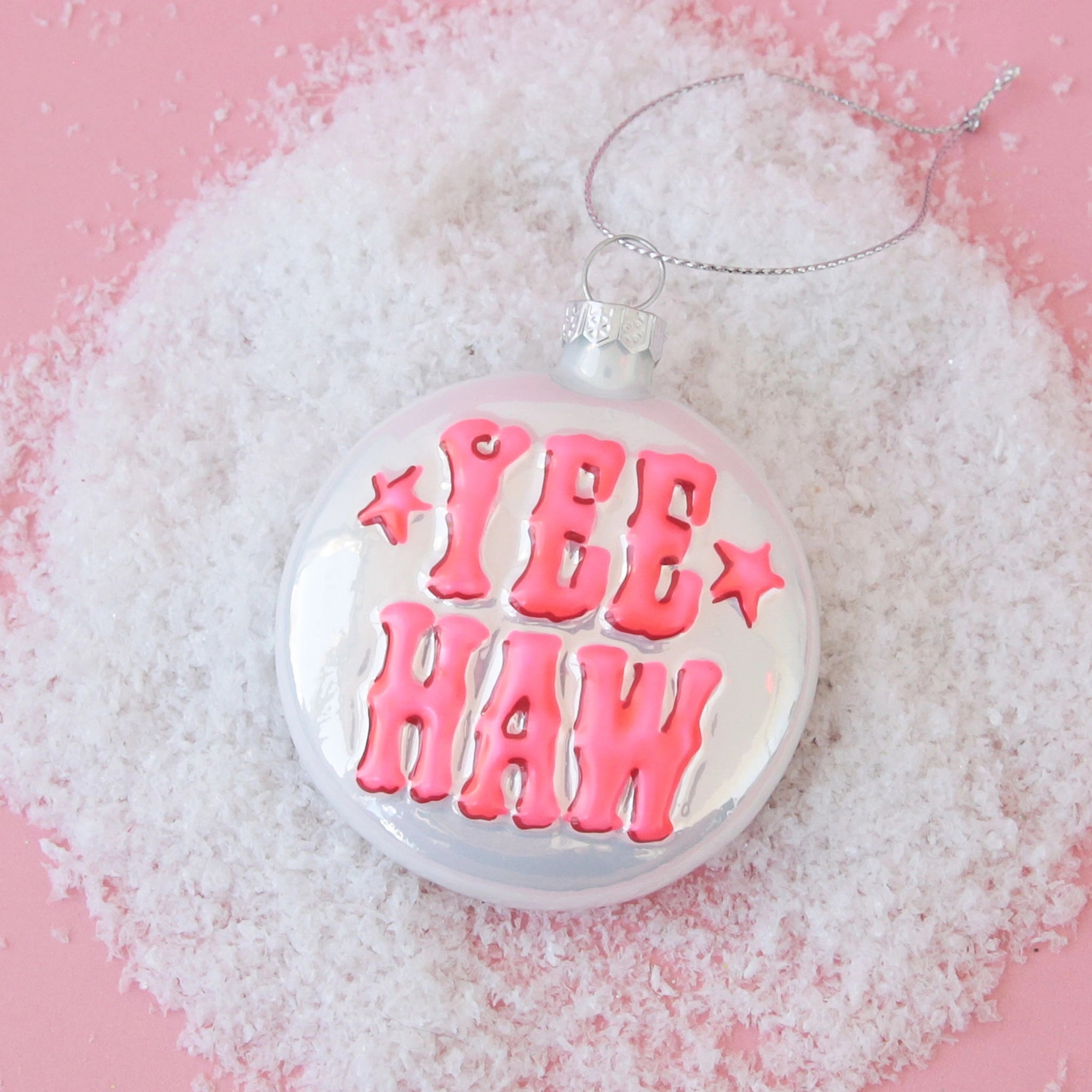 On a pink background is a silver ornament in a round shape with pink western bubble letters that read, &quot;Yee Haw&quot; in pink.