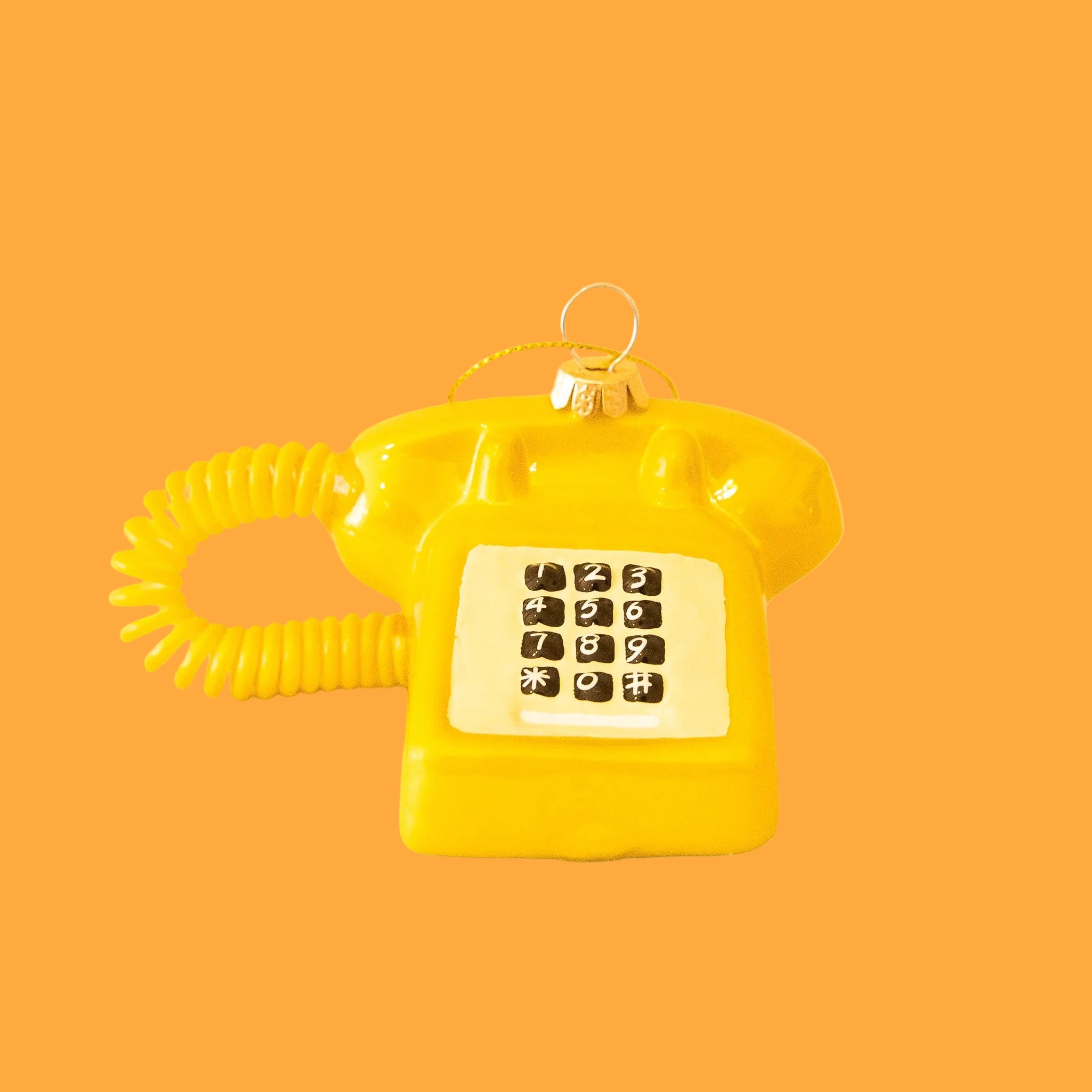 A touch tone glass phone ornament in a shiny gold color on a yellow background. 