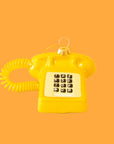 A touch tone glass phone ornament in a shiny gold color on a yellow background. 