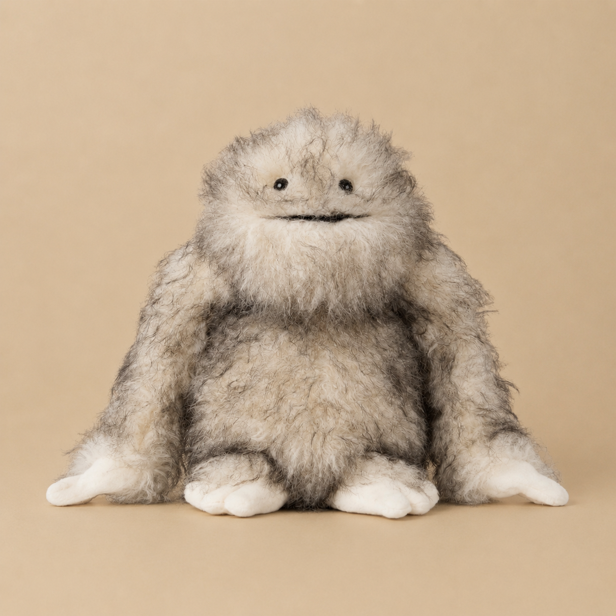 A fluffy gray and white monster plush toy with a stitched face, sitting against a solid beige background.