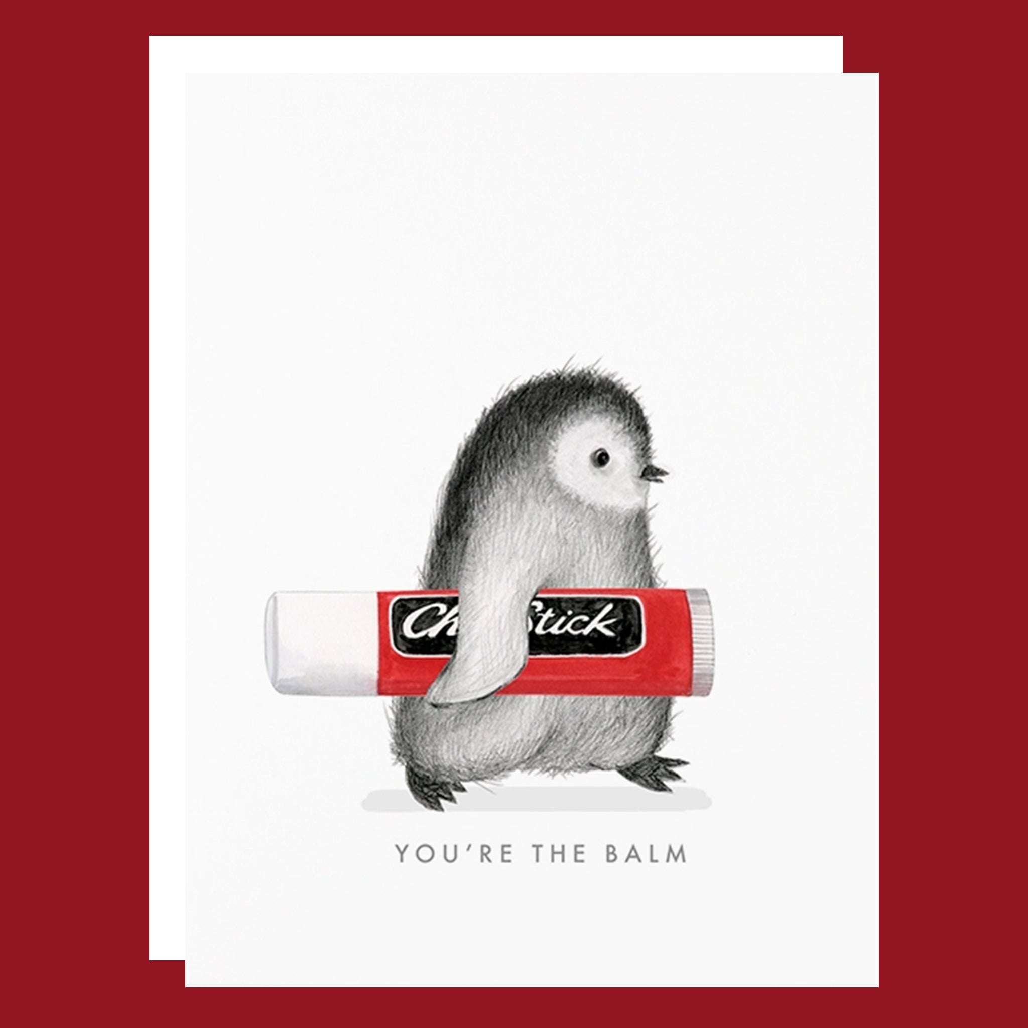 Greeting card with a grey penguin holding a chapstick under his arm. The card reads "You're The Balm". 