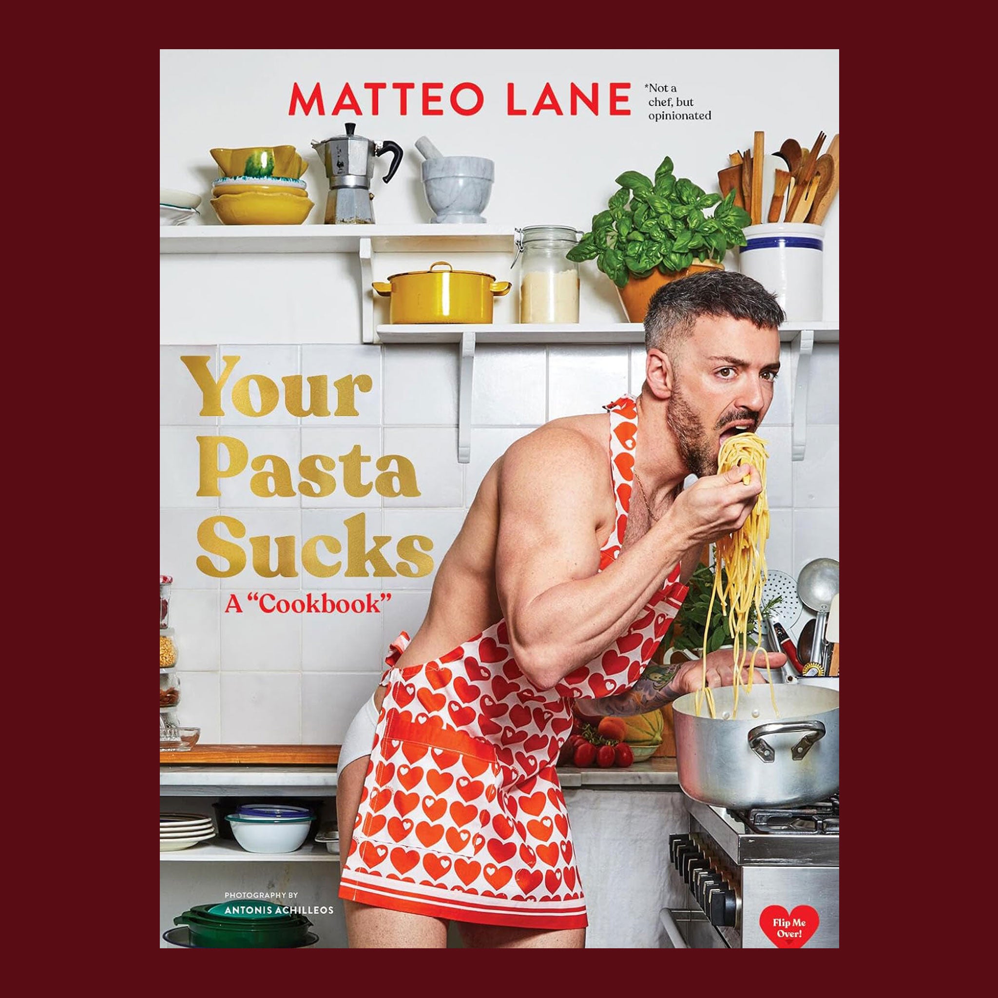 A book cover with Matteo Lane wearing a heart patterned apron and eating pasta with a title that reads, 'Your Pasta Sucks A "Cookbook"'. 