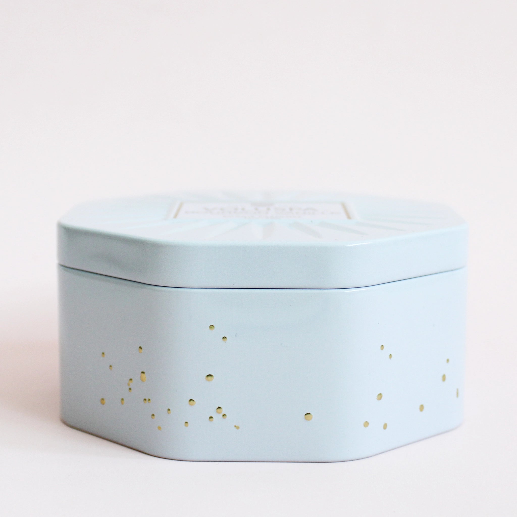 a white with gold speckles octagon shaped tin candle with matching lid. 