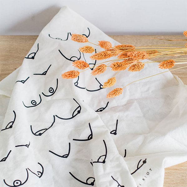 A white tea towel with black line drawings of various boobs in different shapes and sizes. 