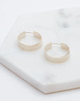 Medium sized silver hoops that have a wider frame and a thin depth. They feature a straight post and a clasp on the back top of the hoop to secure it on your ear.