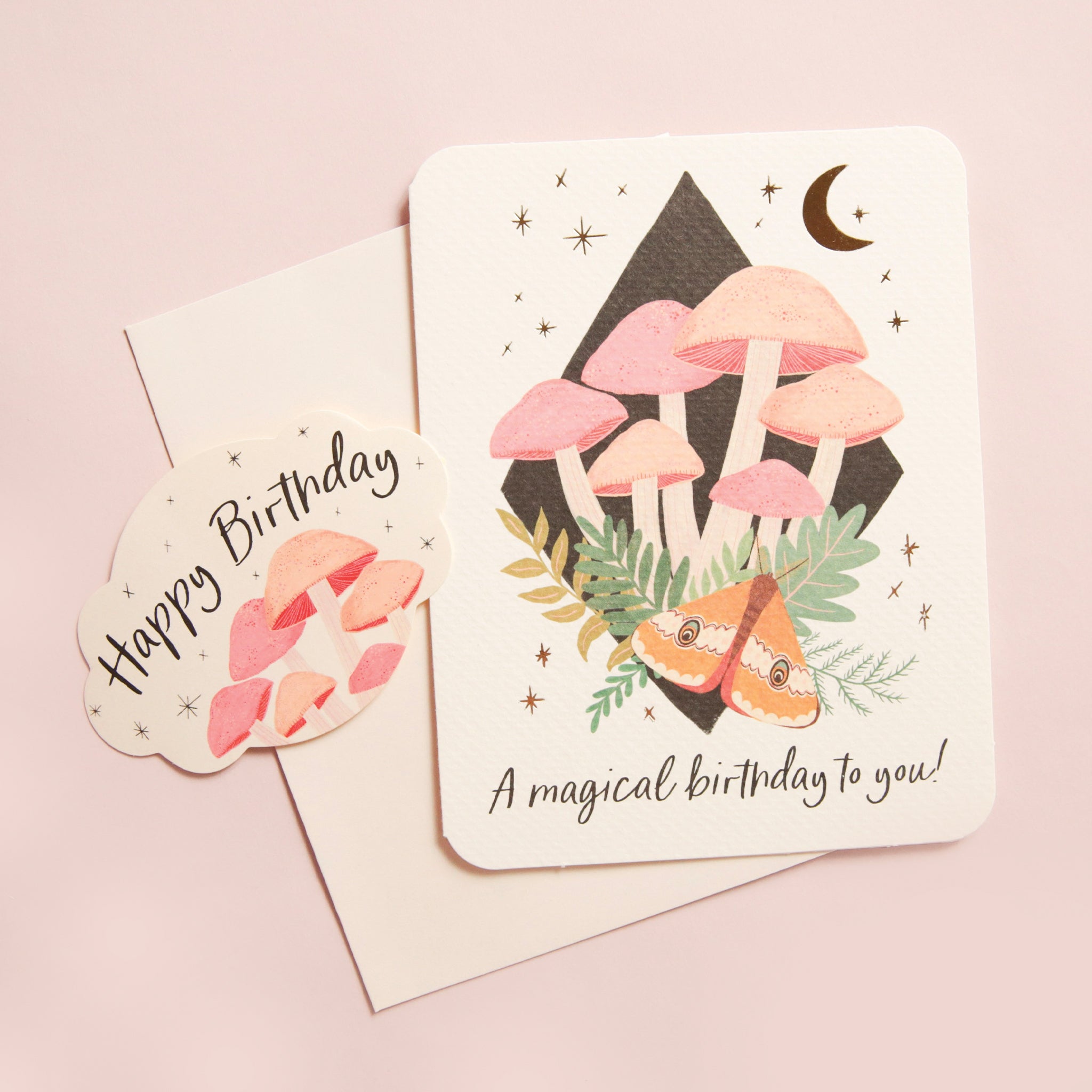 A cream colored card with a graphic of mushrooms, a moth and a moon along with &quot;A Magical Birthday to You&quot;. Also included is a coordinating cream envelope and a mushroom sticker that says, &quot;Happy Birthday&quot;.