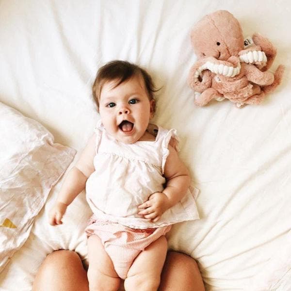 A pink octopus stuffed animal with a smiling face, photographed on a cream background next to a baby model.