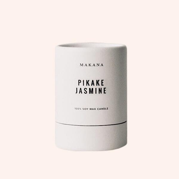 In front of a white background is a white round package. There is black text on the front that reads ‘Makana Pikake Jasmine.&#39;
