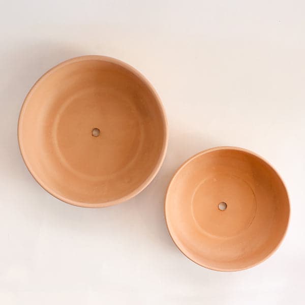 A terracotta ceramic bowl that has a low profile and a wide opening. There are two sizes available and photographed here with a birds eye view showing the drainage hole included.