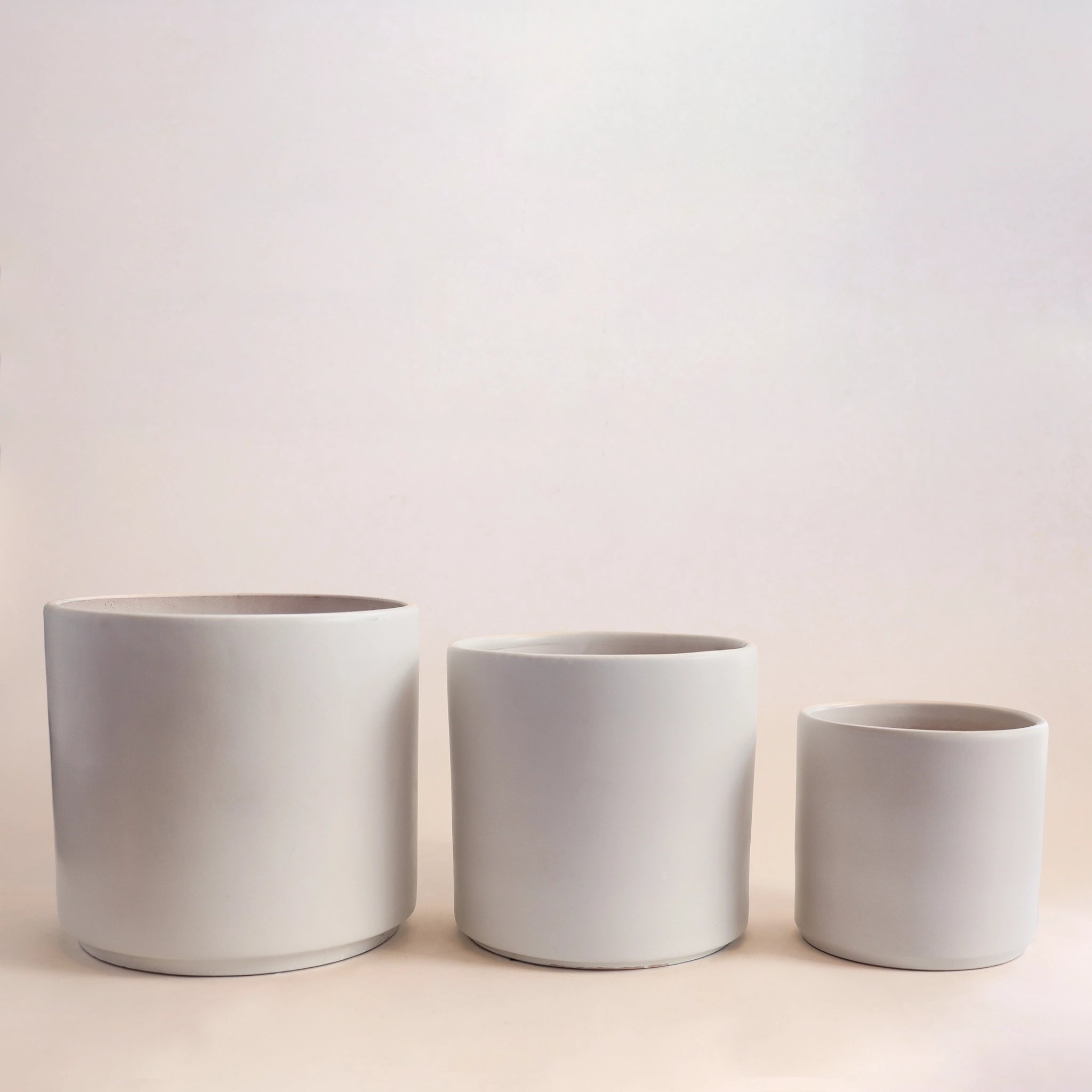 Three different sized white ceramic planters photographed in front of a white background. 