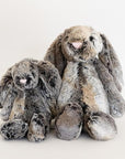 Two, one small and one large, stuffed animals in the shape of mottled grey and gold colored rabbits, with long floppy ears, arms and legs.