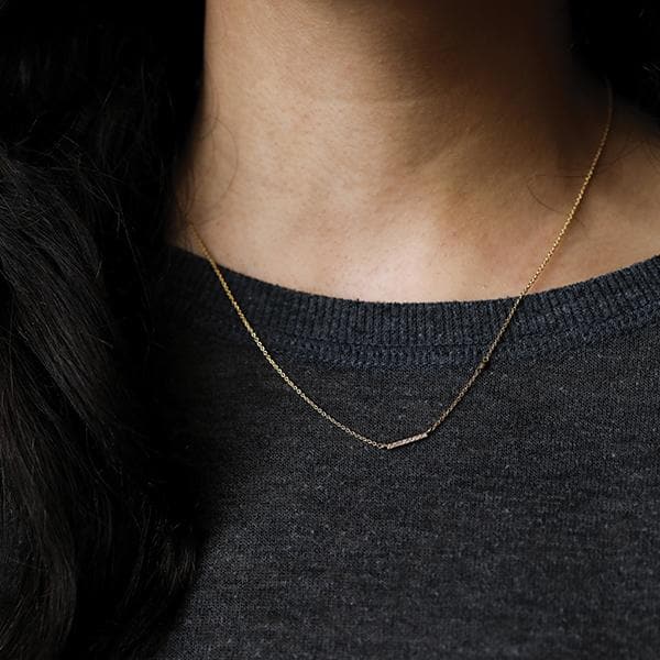 Photo of a woman with dark hair and a dark grey knit top wearing a thin gold necklace with a gold bar and CZ accents.