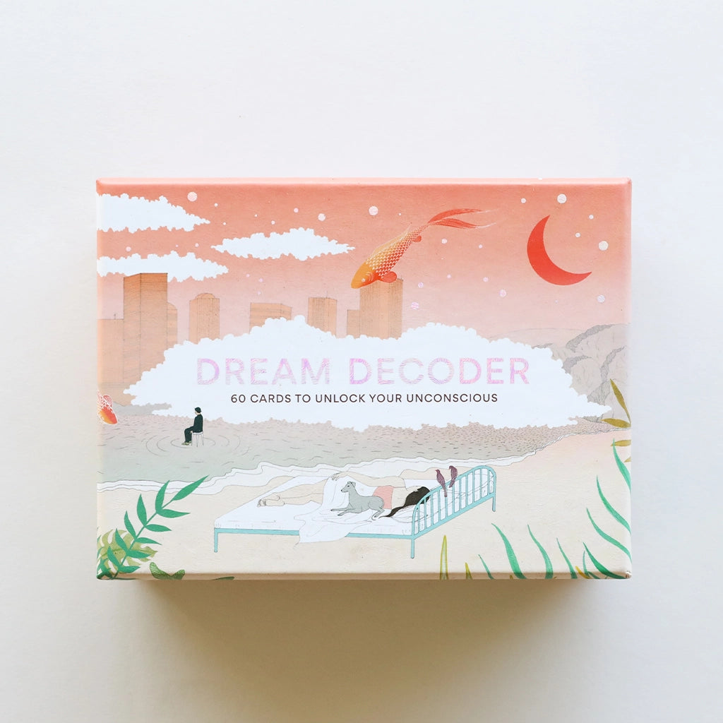 A box with dreamy graphics of the sky and a city with clouds and a bed on the beach. Also photographed are the cards inside of the box that have illustrations of different dream scenarios along with words on the back describing their meaning.