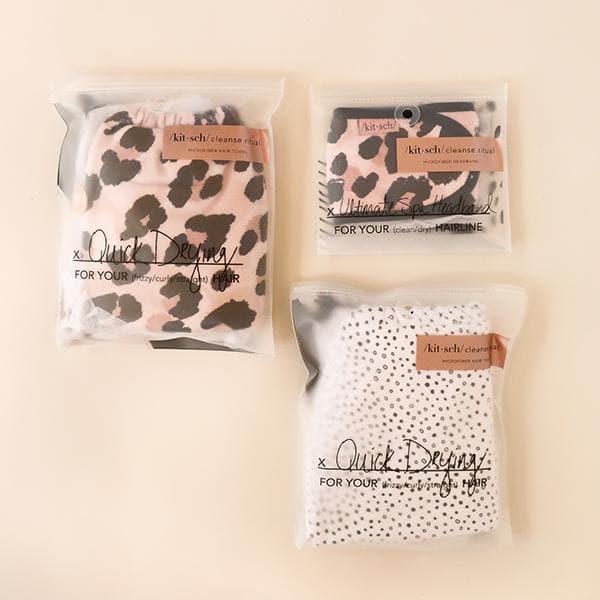 A white microfiber hair towel with tiny black polka dot design all over photographed here in its plastic packaging that reads, &quot;Quick Drying&quot; in black cursive letters across the front alongside other products from the same brand.