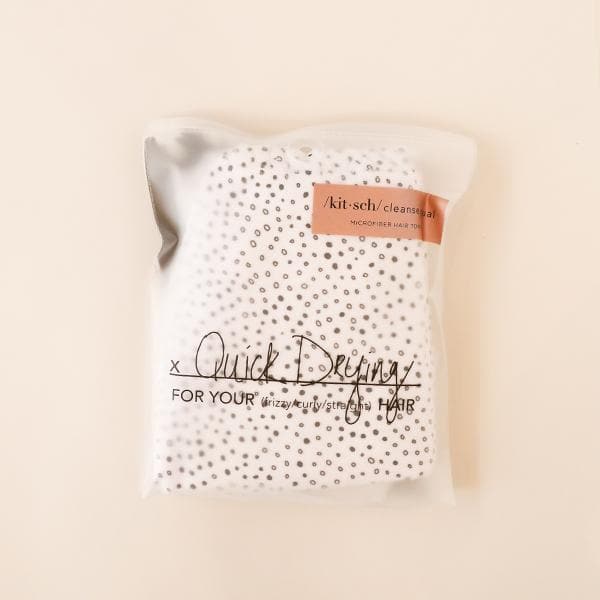  A white microfiber hair towel with tiny black polka dot design all over photographed here in its plastic packaging that reads, &quot;Quick Drying&quot; in black cursive letters across the front.
