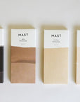 A rectangular bar of chocolate that read, "Mast Milk Chocolate" at the top in black letters along with a two toned wrapper that is brown and white alongside other flavors of chocolate by the same brand that feature different color ways.