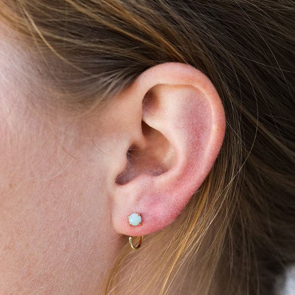A close up of a person wearing gold huggie style earrings with set aqua colored amazonite gem.