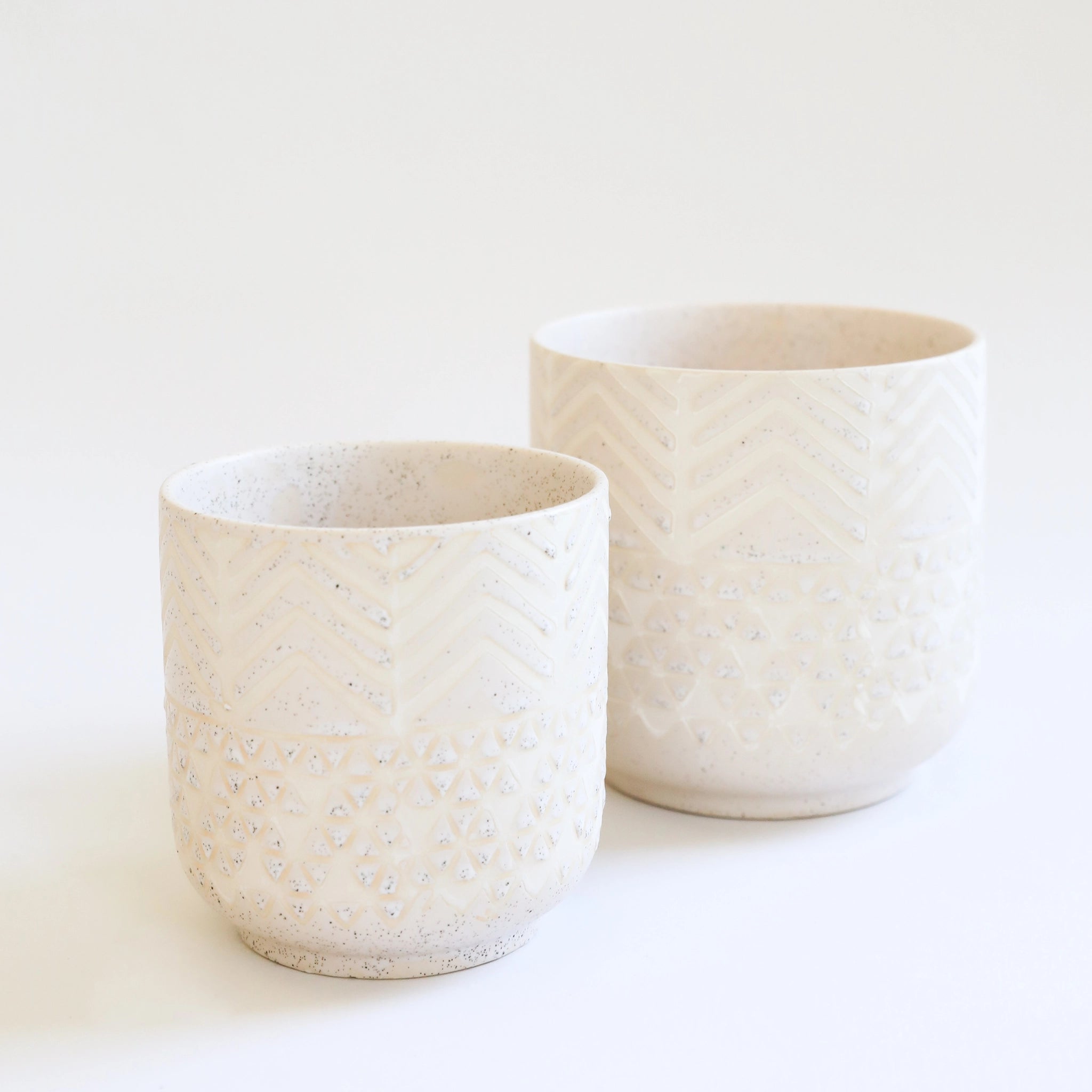 a smaller cream colored pot with chevron detail and speckles sits in front of a larger version of the same pot