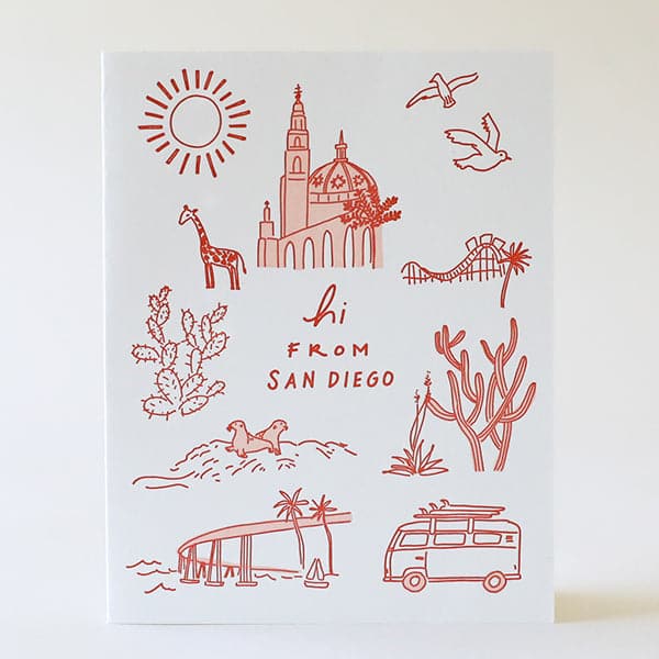 Photo of a greeting card that reads &quot;hi from san diego&quot; in rust letters on a white background. There are also rust colored simple line drawings of San Diego landmarks surrounding the writing, including a sun, the Coronado bridge, La Jolla beach seals, cacti, Balboa Park, and a giraffe representing the zoo.