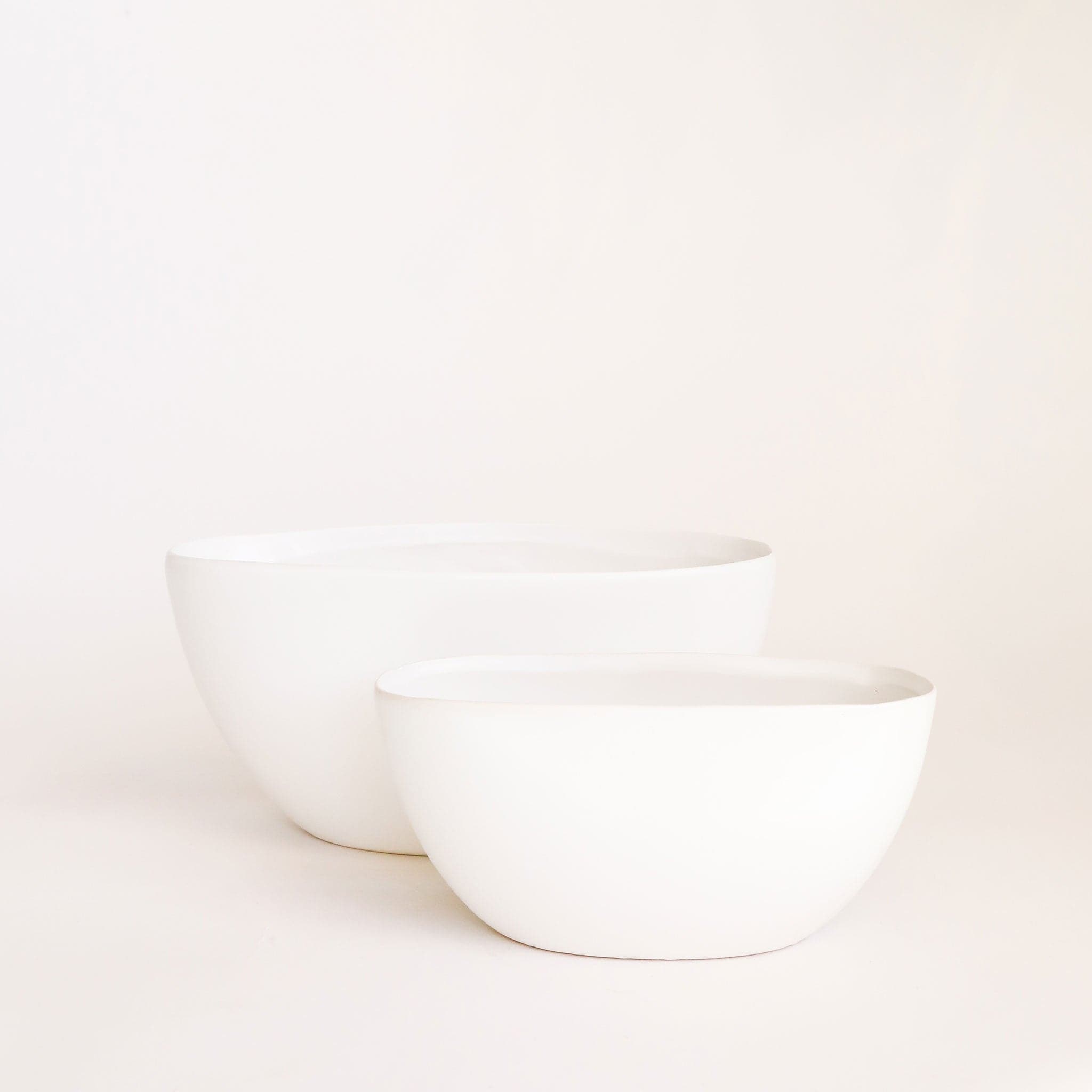 Two white ceramic boat shaped bowls are layered one in front of the other. The front bowl is smaller than the larger placed behind it. 