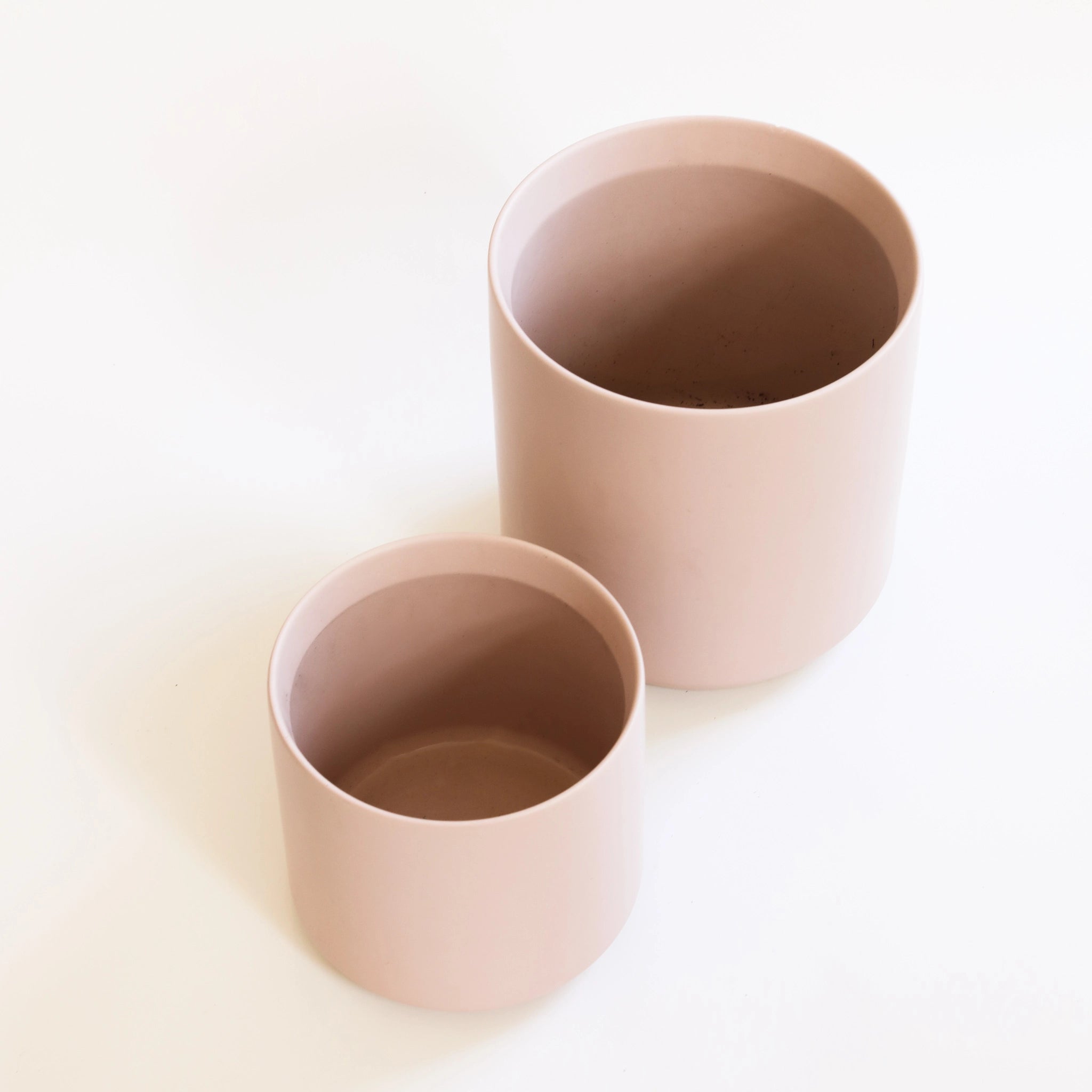 On a cream background is two different sized light pink ceramic planters.