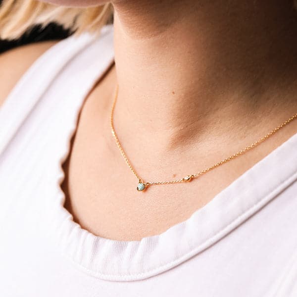 A dainty gold chain necklace with a circular opal stone in the center worn on a model.